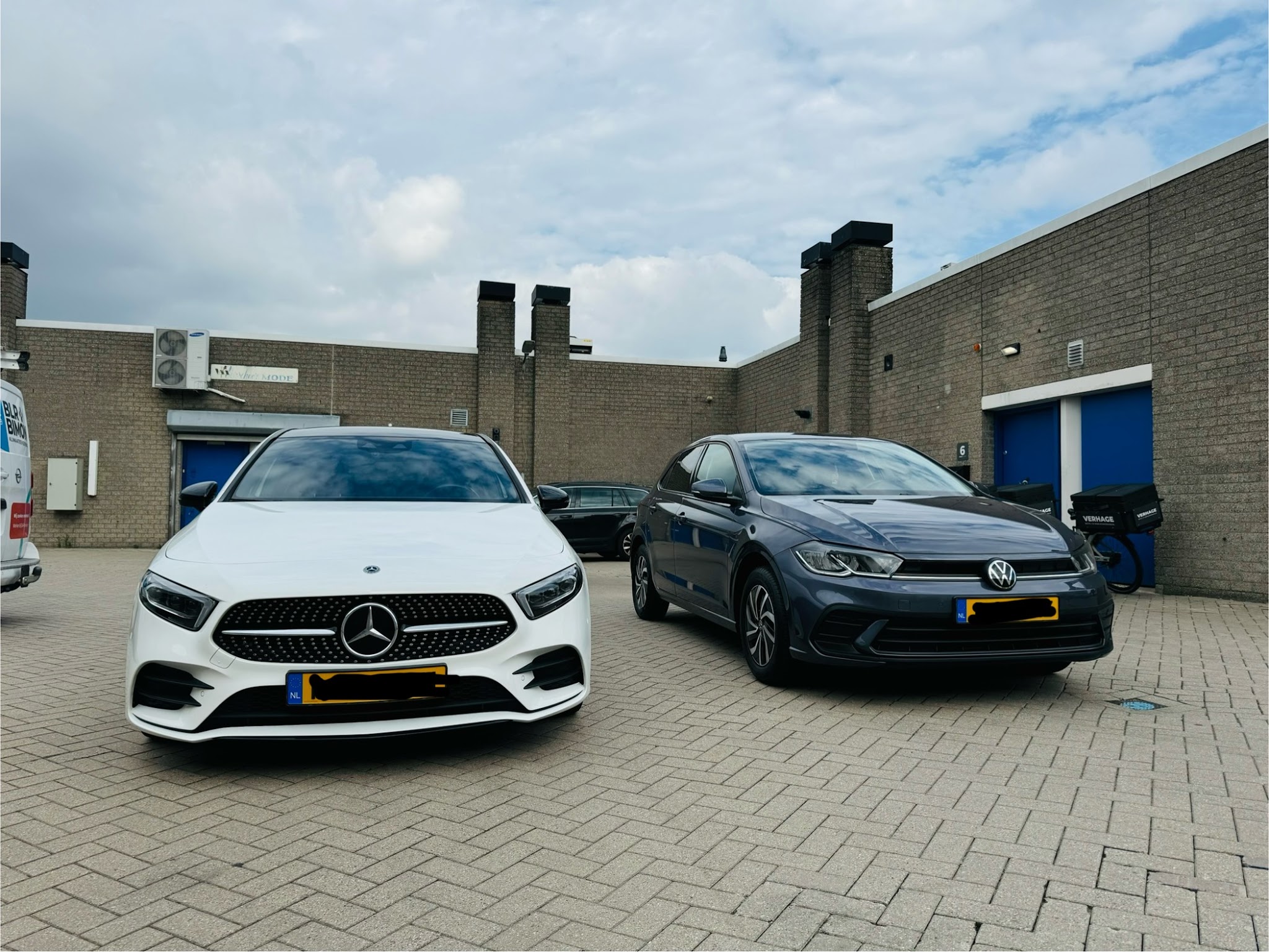 Een witte Mercedes A-klasse en een donkergrijze Volkswagen Polo op het terrein, foto van een klant