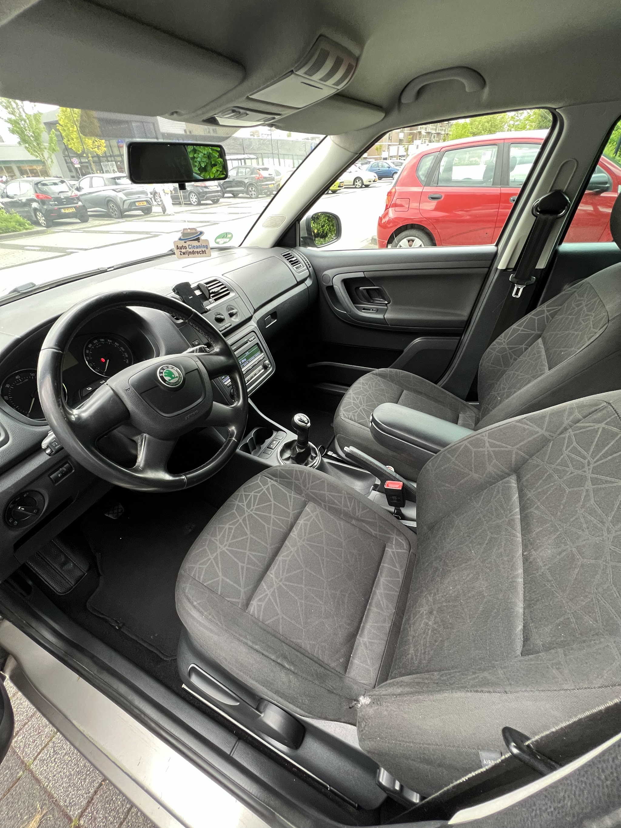 Gereinigd voorinterieur van een Skoda met stuur, dashboard en stoelen, met een Auto Cleaning Zwijndrecht geurhanger aan de spiegel